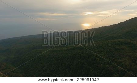 Sunset on tropical island, ocean, mountains, Camiguin. Aerial view coastline on tropical island with sea, trees and palms. Amazingly beautiful landscape of nature with mountains, hills, rain forest. Seascape: Ocean and sky. Aerial panoramic view of island
