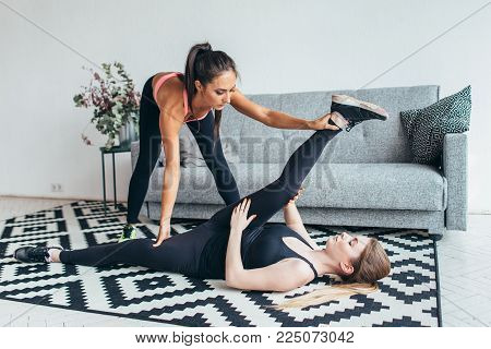 Fit young woman doing stretching exercises with the help of personal trainer at home.