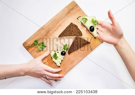 Top virew woman holding fresh avocado and making sandwiches on the table with other ingredients. Healthy living, diet, raw eating, vegetable fats concept background. Selective focus, space for text