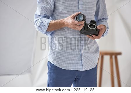 Closeup of male photographer checking lens in modern camera, focus is on hand with lens