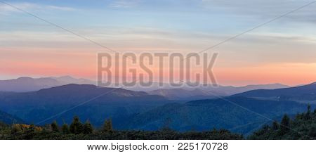Panorama of the mountain ranges covered with forests on the foreground against of a sky in Eastern Carpathians at sunset