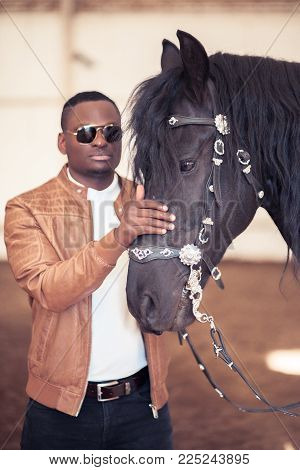African Man Wearing Sunglasses Near A Black Horse In Hangar