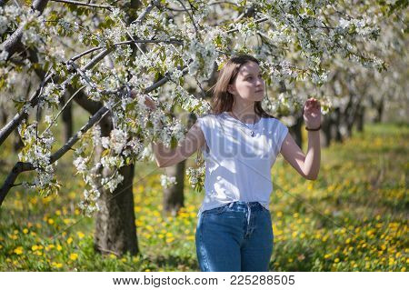 Portrait of a beautiful young girl in a blooming garden against a background of flowering trees on a sunny spring afternoon