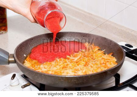 Close up hand adds tomato paste to roasted carrot and cabbage for borscht, vegetable soup