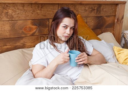 Half Asleep Young Woman Drinking Coffee On Bed