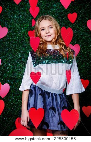 Happy pre-teen girl poses surrounded by little hearts over lawny background. First love. Valentine's Day.