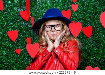 Happy pre-teen girl poses surrounded by little hearts over lawny background. First love. Valentine's Day.