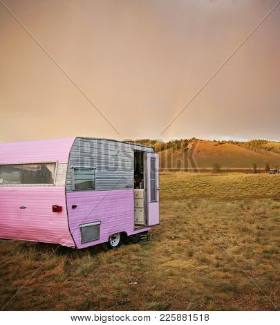 cute vintage camper trailer in the sawtooth mountain range in a desolate camp ground during a summer rain storm with a rainbow in the distance toned with a retro vintage instagram filter 