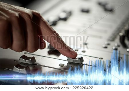 music, technology and equipment concept - male hand moving switch on mixing console in sound recording studio