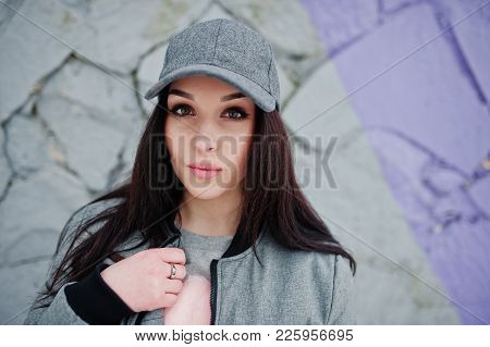 Stylish Brunette Girl In Gray Cap, Casual Street Style On Winter Day Against Colored Wall.