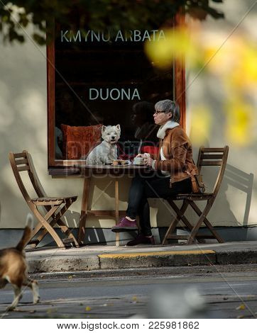 Vilnius, Lithuania - October 7, 2017: Senior Lady Drinks Tea Togeather With Her Dog In Uzupis Distri