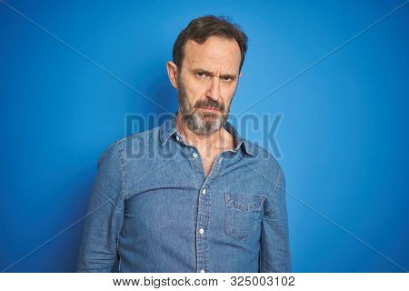 Handsome middle age senior man with grey hair over isolated blue background skeptic and nervous, frowning upset because of problem. Negative person.