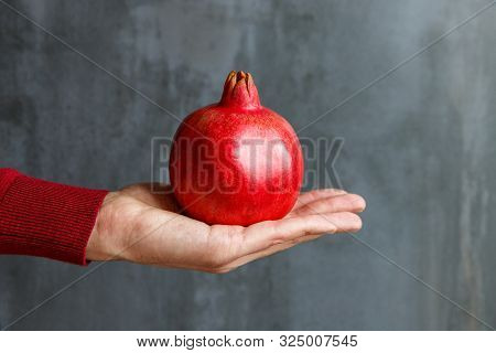 Man Holding In His Hand A Ripe Big Red Pomegranate, Black Stone Background. Pomegranate Fruits Are R