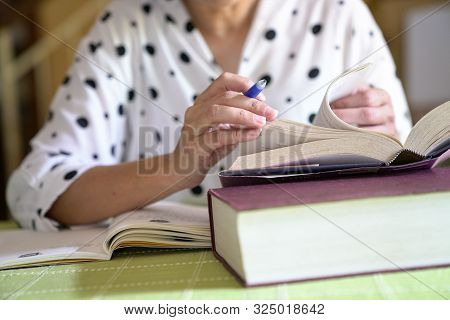 Woman Studying For Her Assignment, Flipping Pages Of A Book While Taking Notes,