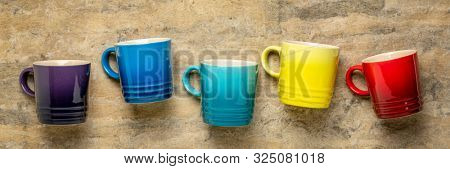 row of colorful stoneware coffee cups against textured handmade bark paper, cofee break concept, long banner