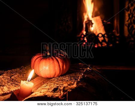 Halloween Pumpkin In The Dark On Birch Logs Next To Burning Candles. In The Background Is A Flame Fr