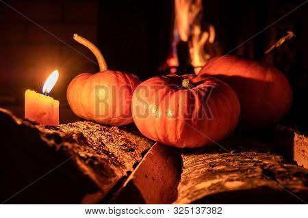 Three Halloween Pumpkins In The Dark On Birch Logs And Burning Candles. In The Background Is A Flame