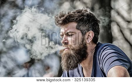 Man Long Beard Relaxed With Smoking Habit. Man With Beard Breathe Out Smoke. Clouds Of Flavored Smok
