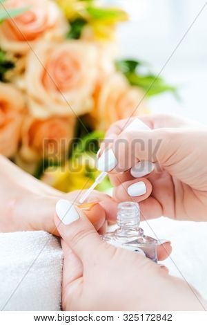 Pedicurist applying white color to foot nails of woman during pedicure