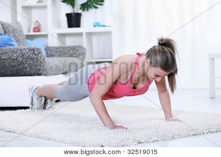 Young woman looking down while doing push-ups in living room