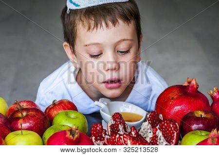 Cute Adorable Jewish Caucasian Boy With A Kippah On His Head Sitting By A Plate Of Split Pomegranate