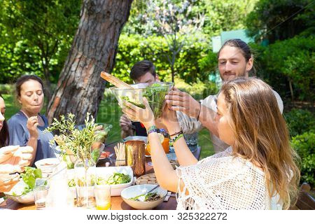 Cheerful Young People At Table In Yard. Happy Young Male And Female Friends Gathering Around Table W