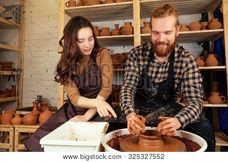 A Bearded Man And A Young Woman Mold A Vase Of Clay On A Potters Wheel Near The Rack With Vases And 
