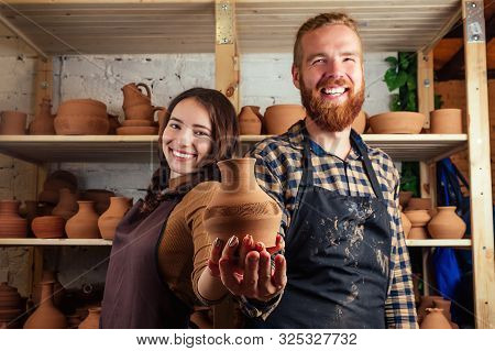 A Bearded Man And A Young Woman Holding A Vase Of Clay And Having Fun Near The Shelf With Vases And 