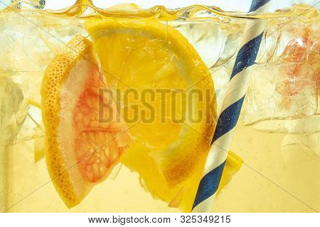 Close Up Of Lemon Slices In Stirring The Lemonade And Ice Cubes On Background. Texture Of Cooling Sw