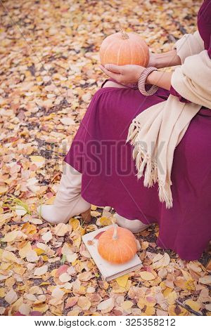 A Woman In A Lilac Dress With A Scarf Sits In An Autumn Park Among The Fallen Yellow Leaves And Hold