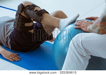 Pretty Patient Sitting On The Blue Mat In The Gym And Training With The Ball