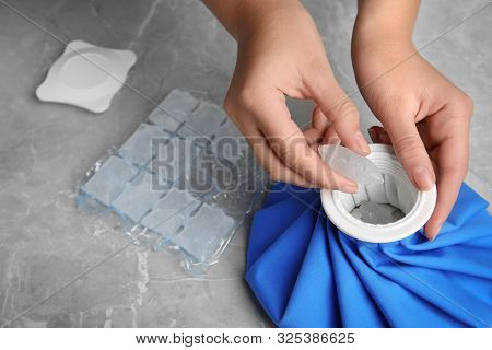 Woman Putting Ice Cubes Into Pack At Marble Table, Closeup