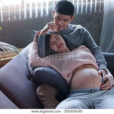 The Pregnant Woman Laying Down On Sofa And Hugging By Her Husband,put Hand Touch Belly,waith For New