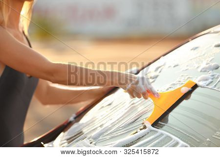 Young Woman In Swimsuit Washing Windshield Of Car With Squeegee Outdoors, Closeup