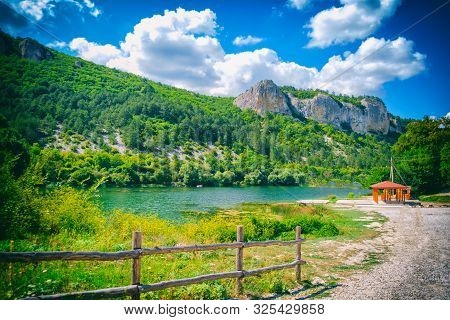 Lake At The Foot Of The Mountain. In The Background Is A High Mountain And Blue Sky With Clouds.