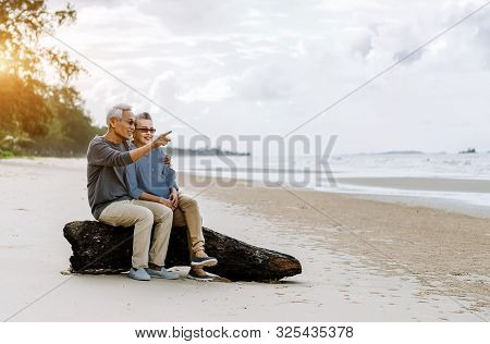 Asian Senior Couple Or Elderly People Walking And Siting At The Beach On Their Weekend Vacation Holi
