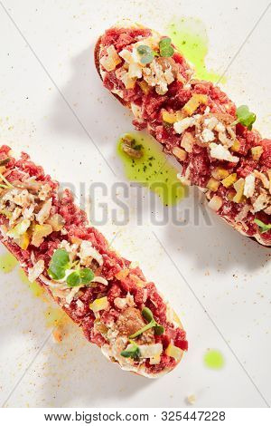 Exquisite serving beef tartare on toast with pickles and black garlic cream on white restaurant plate isolated. High cuisine restaurent dish, minced veal steak meat in minimalist style