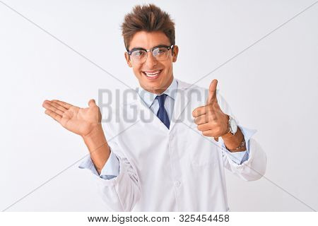 Young handsome sciencist man wearing glasses and coat over isolated white background Showing palm hand and doing ok gesture with thumbs up, smiling happy and cheerful