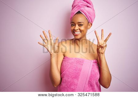 African american woman wearing shower towel after bath over pink isolated background showing and pointing up with fingers number eight while smiling confident and happy.