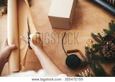 Hands Cutting Wrapping Paper With Scissors And Gift Box, Pine Branches, Cones, Gingerbread Cookies,