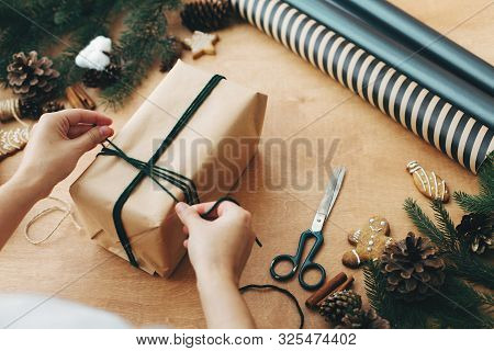 Hands Wrapping Rustic Christmas Gift, Tying Green Twine ,and Pine Branches, Cones, Gingerbread Cooki