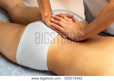 Close Up Of Physiotherapist Applying Pressure On Tailbone Of Female Patient.