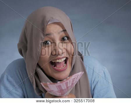 Portrait Of Indonesian Muslim Woman Holding Rupiah Money, Smiling Laughing Winning Gesture