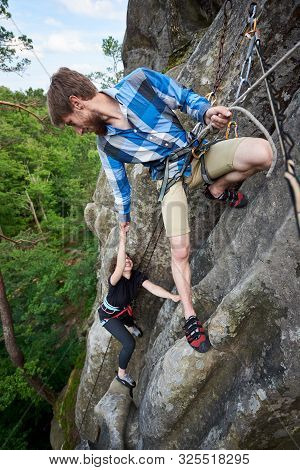 Man Hiker Climbing Overhanging Rock With Rope. Man Helping His Friend Bouldering. Helping Hand. Tour