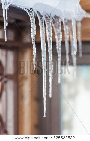 Icicles That Hang From The Roof Of A Wooden House In Winter.