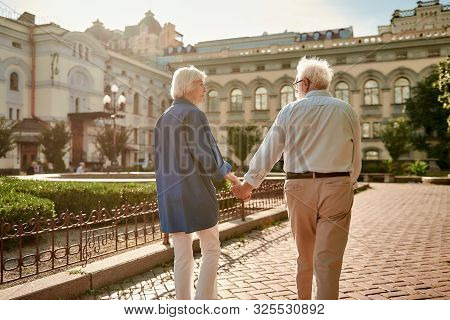 I Want To Travel With You. Back View Of Elderly Couple Holding Hands While Walking Together Outdoors