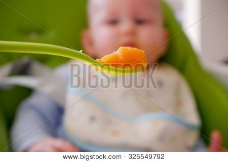 Spoon Full Of Carrot Pure And A Blurry Baby On Background. Selective Focus On The Spoon. Baby First