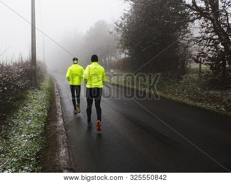 Two Athletic Young Man Running In The Winter Nature.