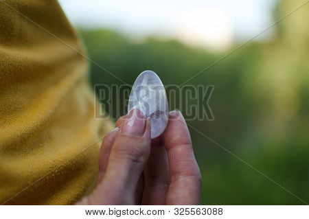 Adult Girl In Yellow Shirt And Blue Jeans Is Holding Transparent Violet Amethyst Yoni Egg For Vumfit