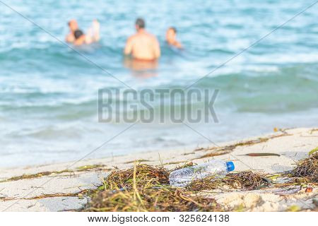 Close Up Image Of Empty Plastic Water Bottle On Dirty Beach Filled With Seaweed, Garbage And Waste O